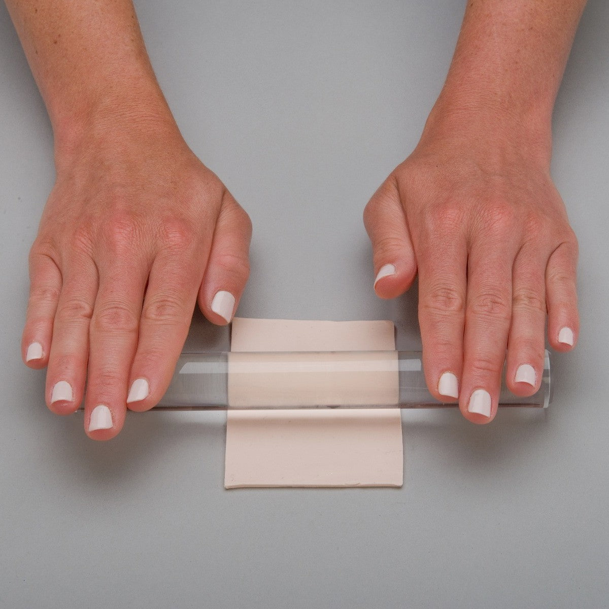Hands holding a clear acrylic rolling pin and using it to roll clay. Sculpey.