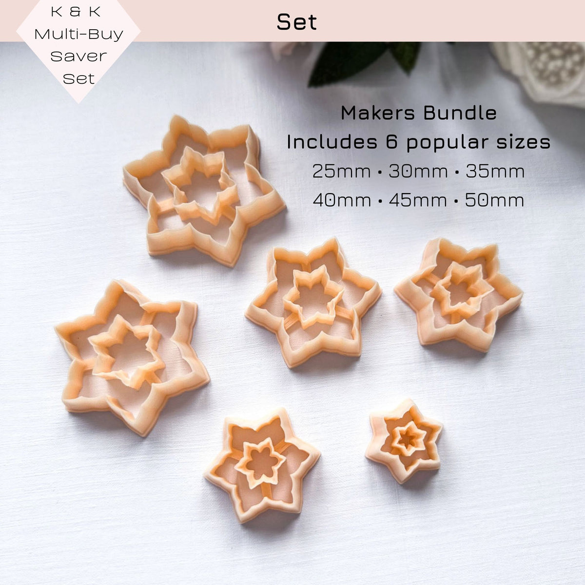 Set of peach-colored star snowflake-shaped cookie clay cutters sits on a white surface, with green plant leaves in the upper left corner. The set is a multi buy saver set with 6 sizes 25,30,35,40,45,and 50mm