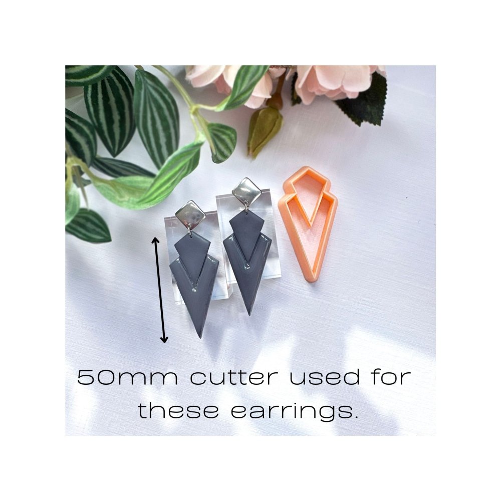Art deco dagger polymer clay earrings on a white surface with green leaves in the background. made with the dagger clay cutter - 50mm