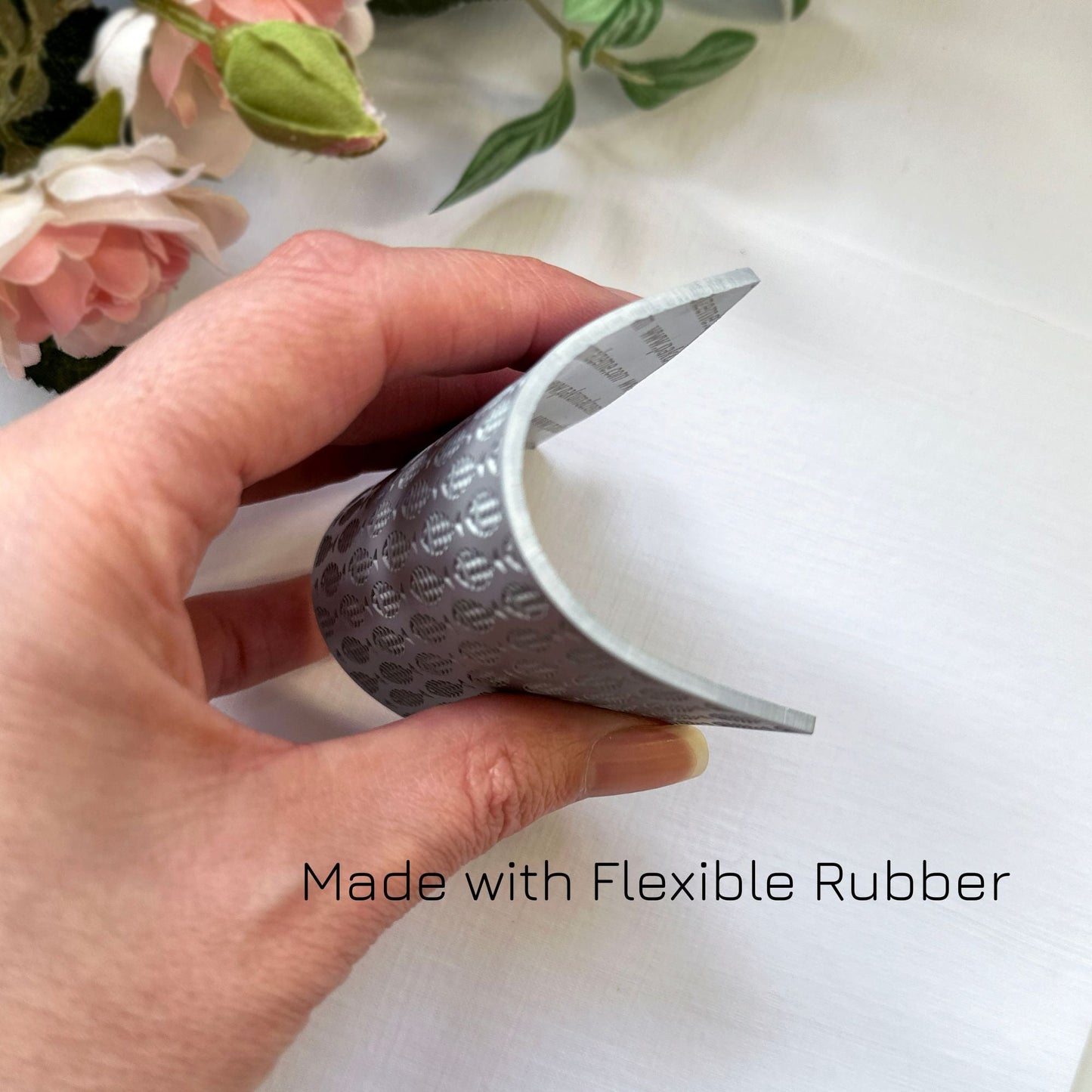 Hand showing flexibility of a texture stamp with a school-of-fish print against a light background with flowers.