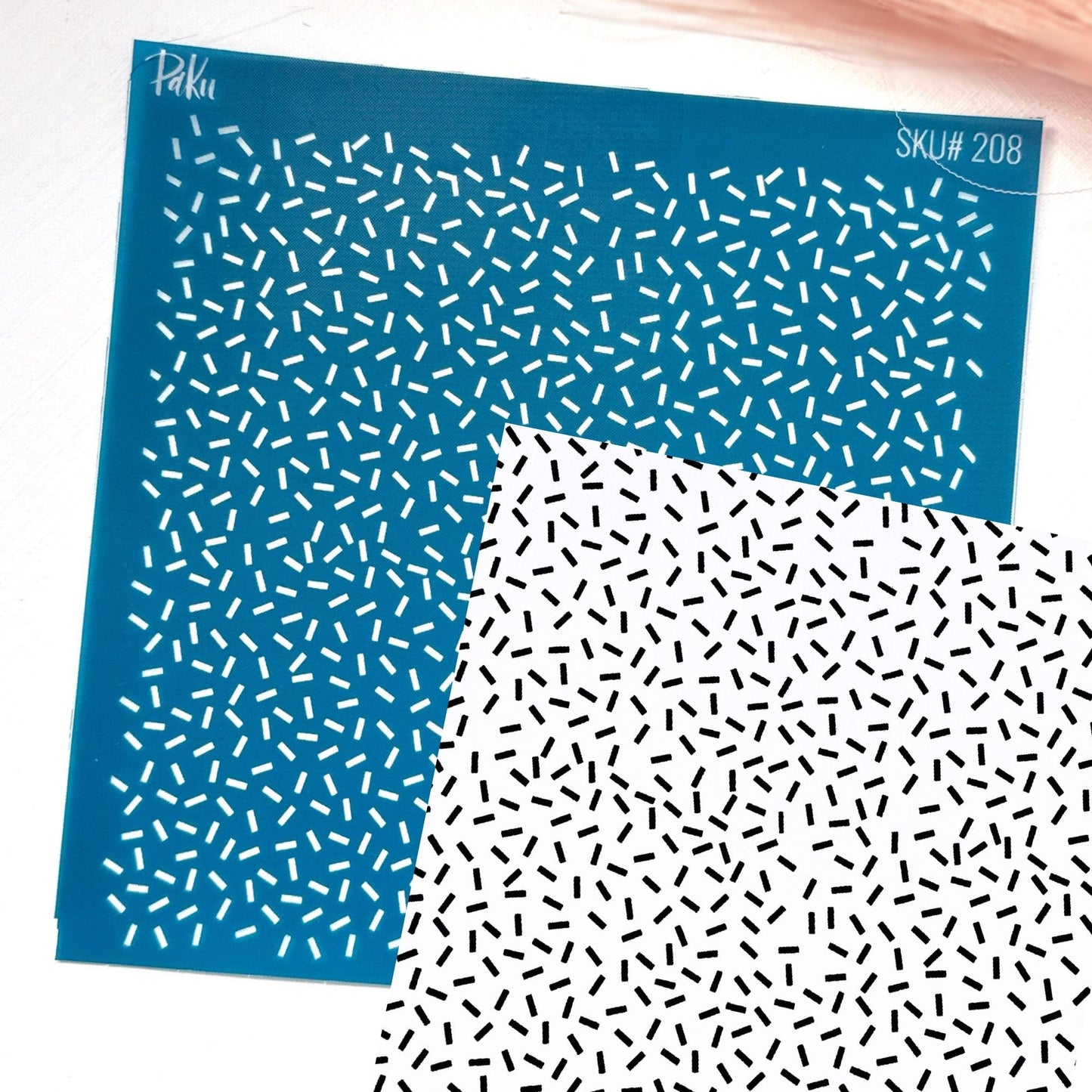 A blue silkscreen stencil sheet with a repeating pattern of small white dashes, sprinkles, shown overlapping a white sheet with a black dash pattern. The stencil has the brand name 'Paku' and SKU text 'SKU# 208' printed on it.