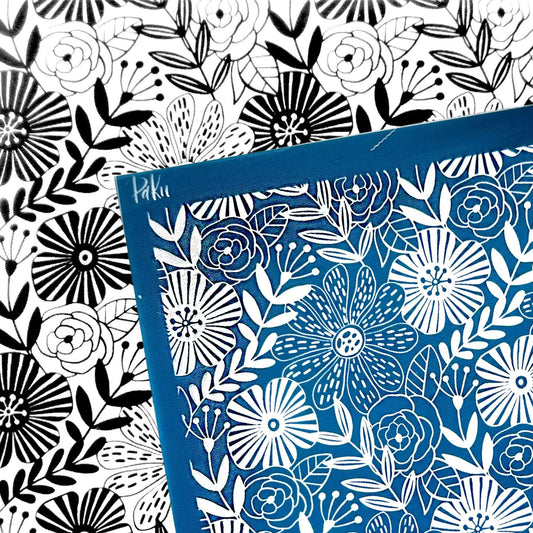 A square blue card or silkscreen stencil with a white floral line-art pattern, placed over a black-and-white floral patterned background. The blue card has a small visible brand mark reading 'Hikaru' in the upper left corner.