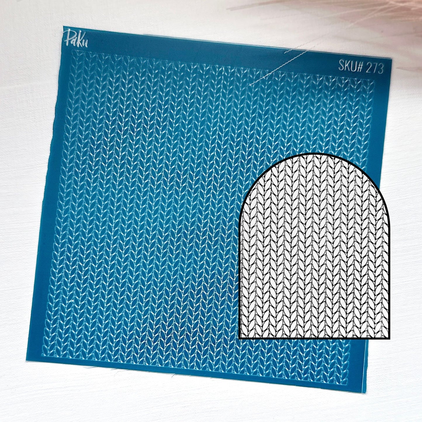 A blue knitting pattern silkscreen stencil sheet with a repeating knit stitch design and a black-and-white circular inset showing the pattern motif. The sheet has the brand name 'Piku' and SKU 'SKU# 273' printed on it, set against a light textured background.