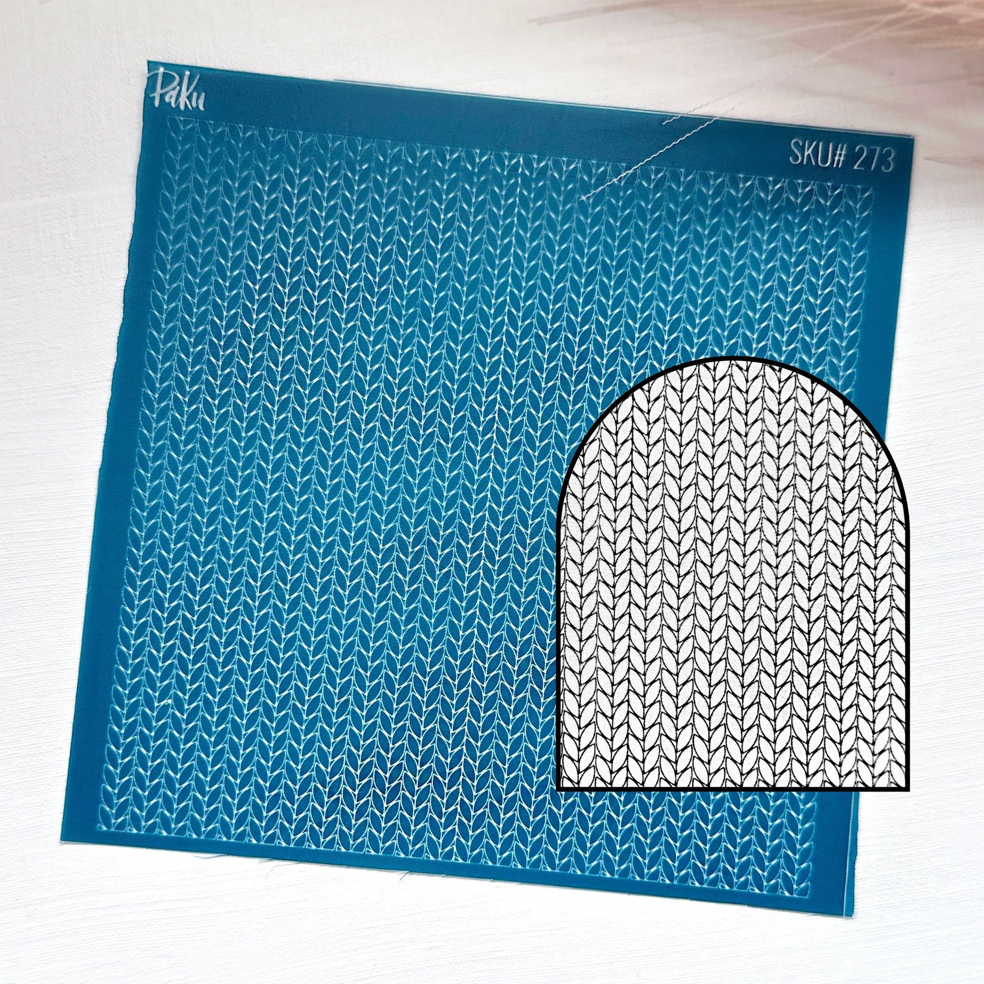 A blue knitting pattern silkscreen stencil sheet with a repeating knit stitch design and a black-and-white circular inset showing the pattern motif. The sheet has the brand name 'Piku' and SKU 'SKU# 273' printed on it, set against a light textured background.
