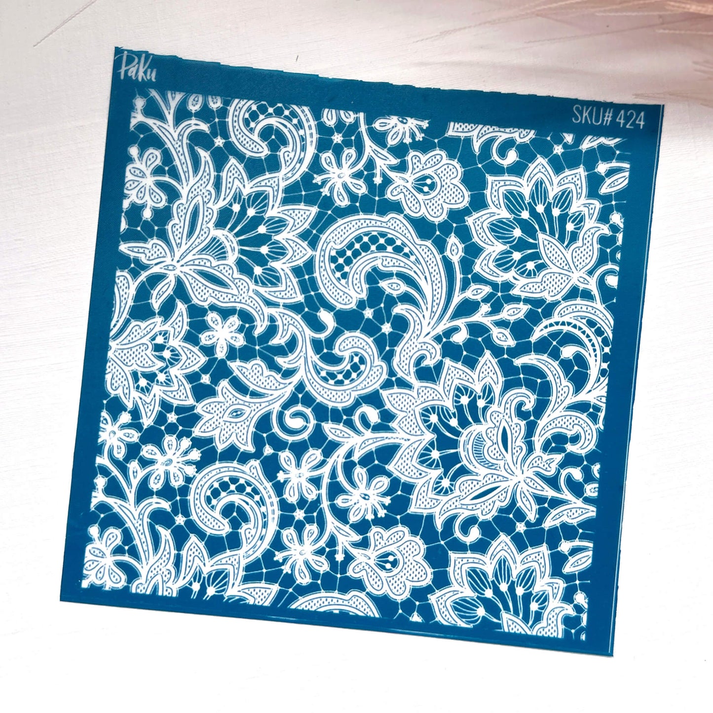 A square blue silkscreen stencil or template with an intricate white floral and paisley cutout pattern, shown on a light wood background. The stencil features the brand name 'Haku' in the top-left corner and the SKU code 'SKU#424' in the top-right corner.