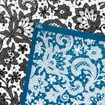 A blue and white lace silkscreen stencil sheet with a floral and paisley pattern, shown overlapping a black and white lace sheet. The brand name 'Paku' is visible in white script on the blue border.lkscreen 
