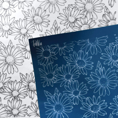 A blue rectangular silkscreen stencil sheet with white daisy outlines, placed over a white sheet featuring matching black-and-white daisy line drawings. The blue sheet appears to be the product being sold rather than an auxiliary chart.