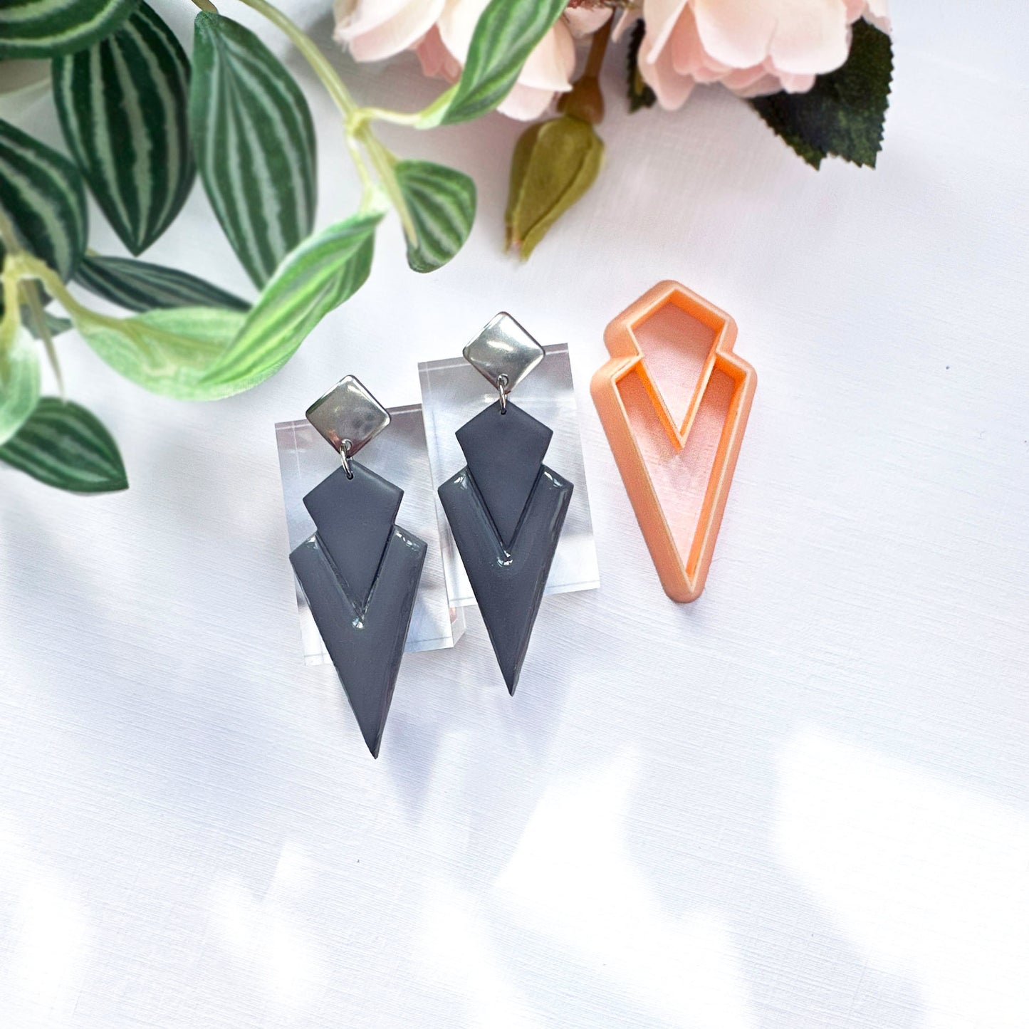 Art deco dagger polymer clay earrings on a white surface with green leaves in the background. made with the dagger clay cutter 