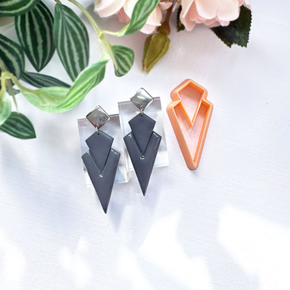 Art deco dagger polymer clay earrings on a white surface with green leaves in the background. made with the dagger clay cutter 
