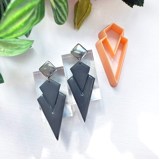 Art deco dagger polymer clay earrings on a white surface with green leaves in the background. made with the dagger clay cutter 