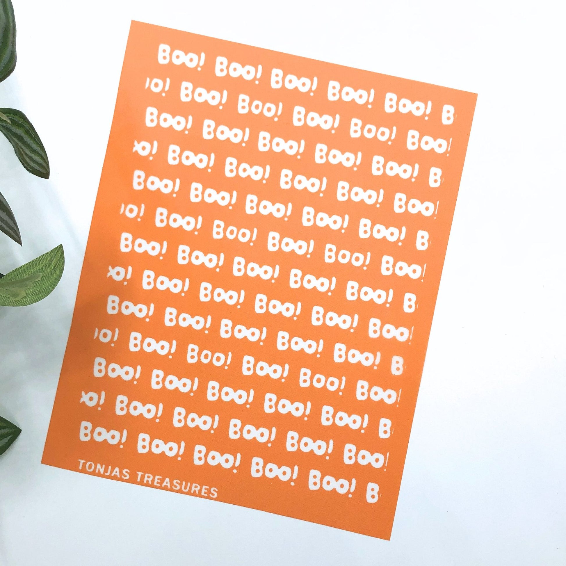 An orange silkscreen sheet featuring the word 'Boo!' repeated in white in various sizes, with 'TONJAS TREASURES' printed at the bottom left, shown on a white background with green leaves on the side.