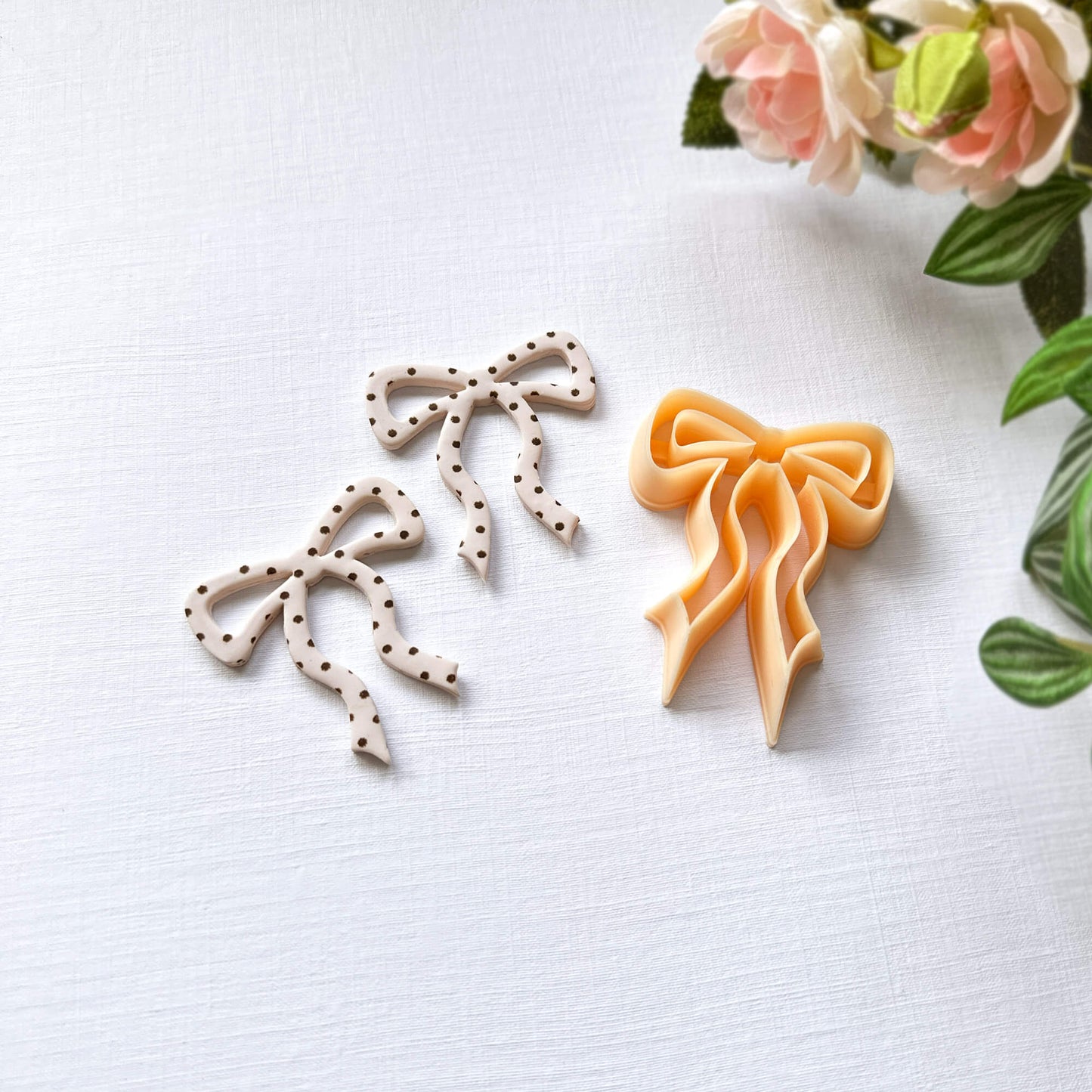 bow-shaped polymer clay cut-out on a light surface with the clay cutter in the front and a plant in the background