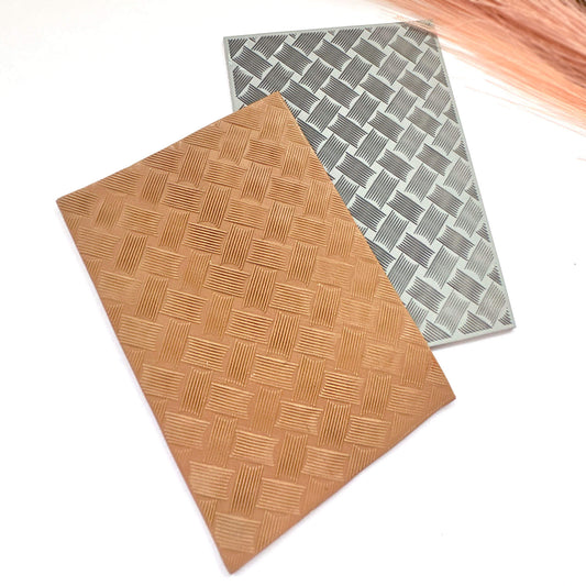 A polymer clay stamped impression in warm tan/caramel with a basketweave pattern. A textured rectangular stamp in grey with a woven pattern sits behind on a white background.