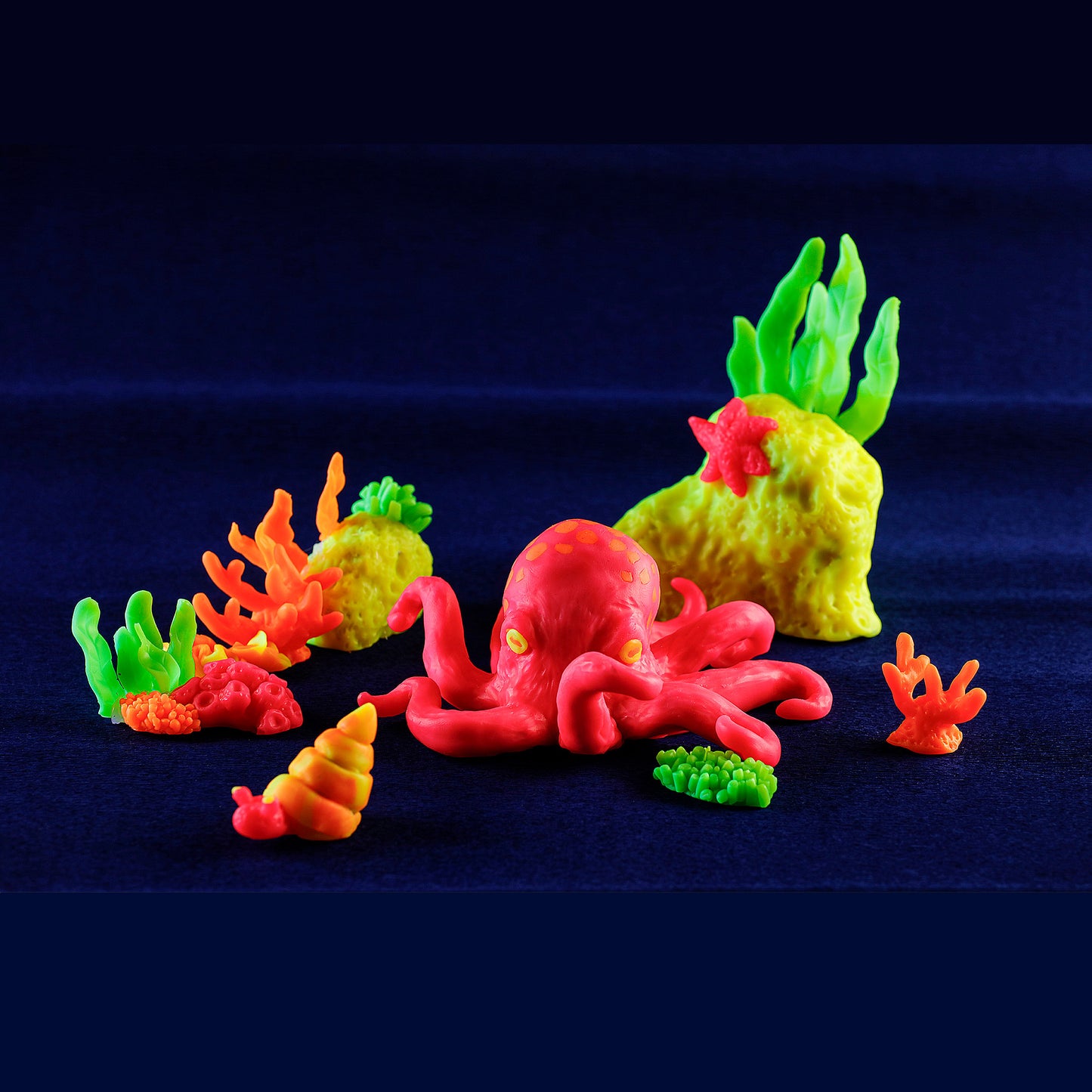 Colorful plastic octopus and coral toys made from cernit neon polymer clay -glowing on a dark blue background