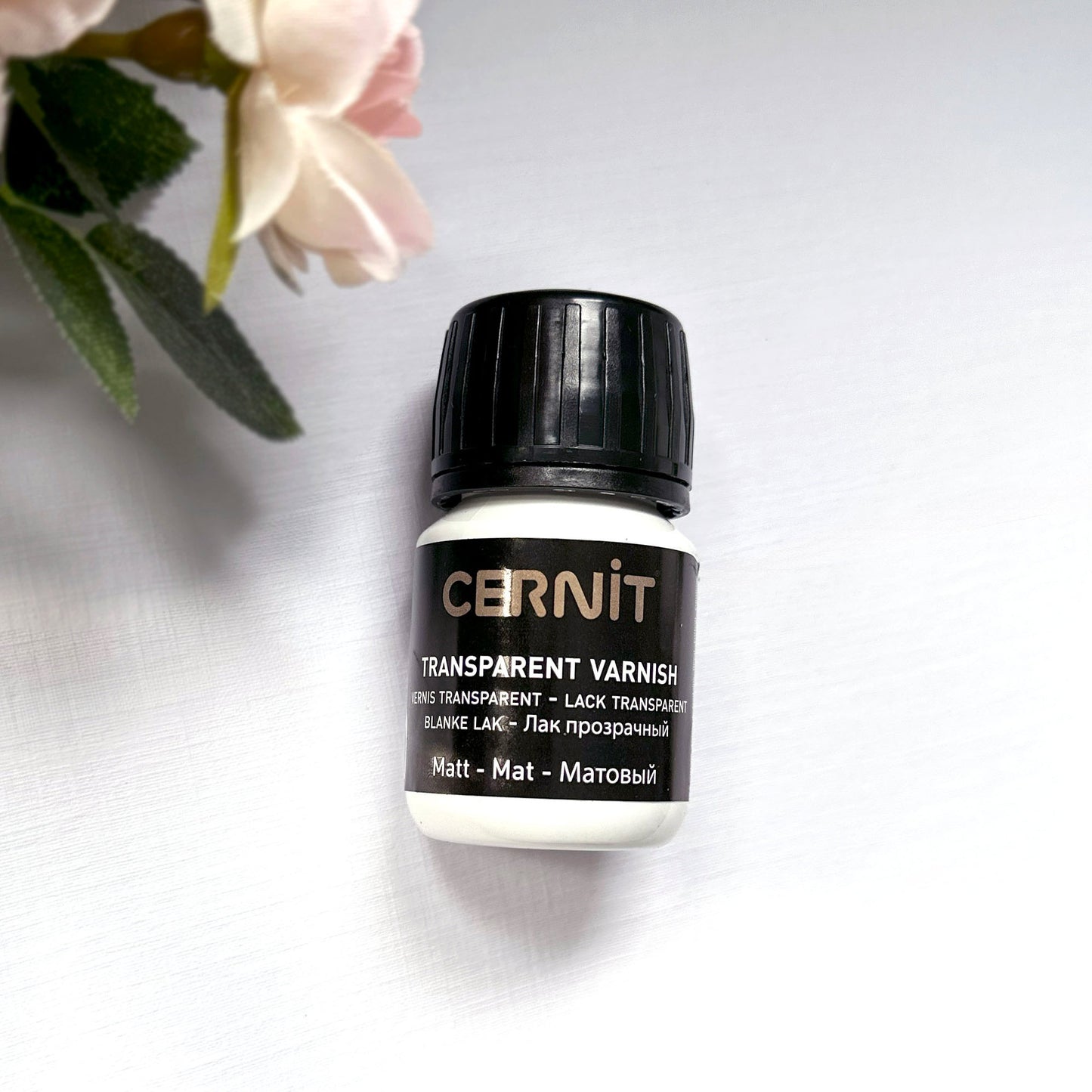 Cernit transparent varnish bottle on a light background with flowers - matt