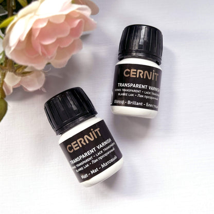 Two bottles of CERNIT transparent varnish on a light background with flowers.