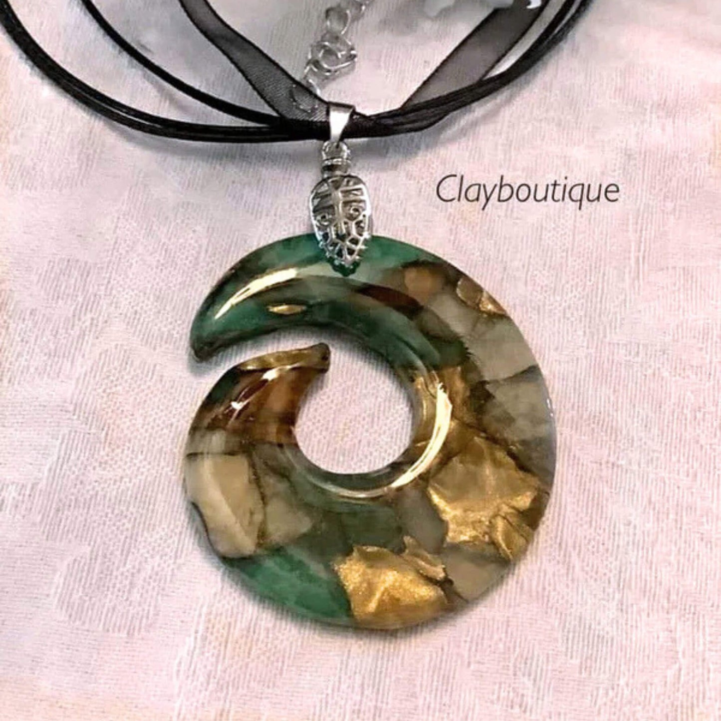 Necklace with a circular pendant featuring gold and green colors on a light fabric background.