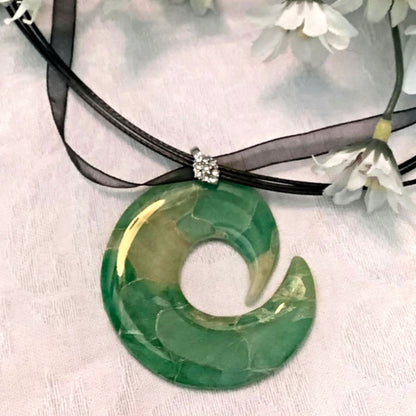 Green stone pendant on a black cord with white flowers in the background