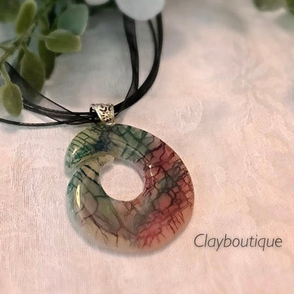 Colorful pendant necklace on a light fabric background with 'Clayboutique' branding.
