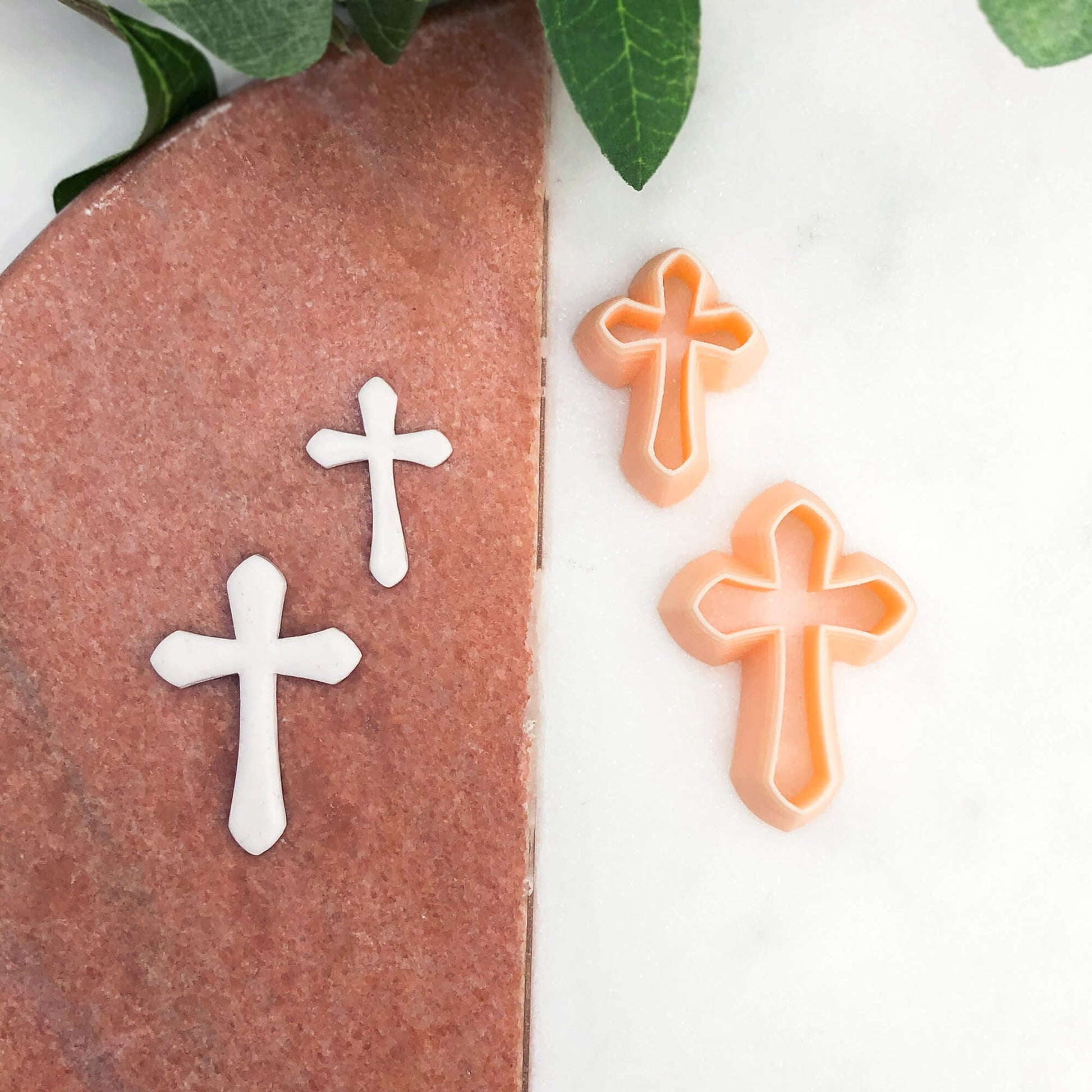 cross clay cutter x 2 with the polymer clay cut outs on a pink and white marble background
