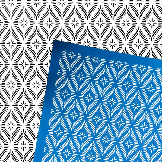 A blue rectangular silkscreen stencil with a white repeating geometric star-and-diamond pattern, placed diagonally over a black-and-white patterned background. 