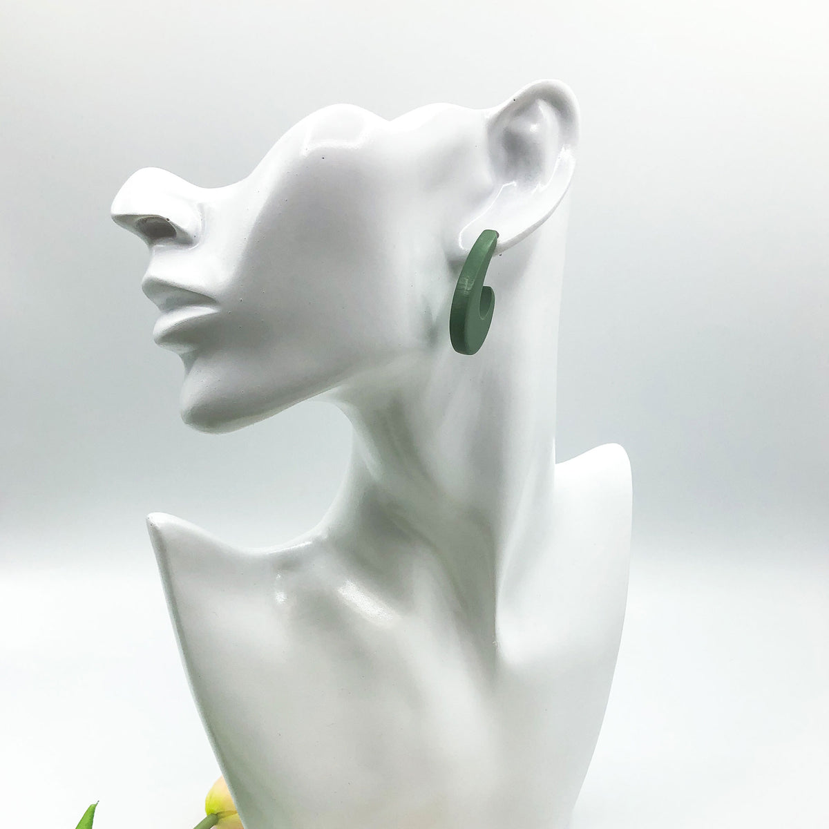 A dark green curved hoop earring displayed on a white ceramic female bust against a light gray background.