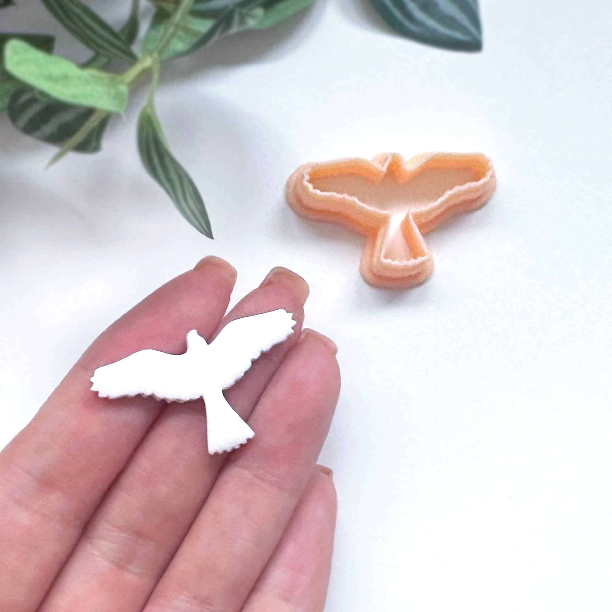 White bird-shaped polymer clay cut out with the eagle clay cutter on the side.  Eagle held in a hand with a green leafy background.