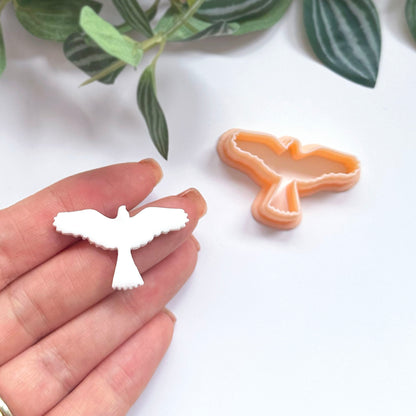 White bird-shaped polymer clay cut out with the eagle clay cutter on the side.  Eagle held in a hand with a green leafy background.