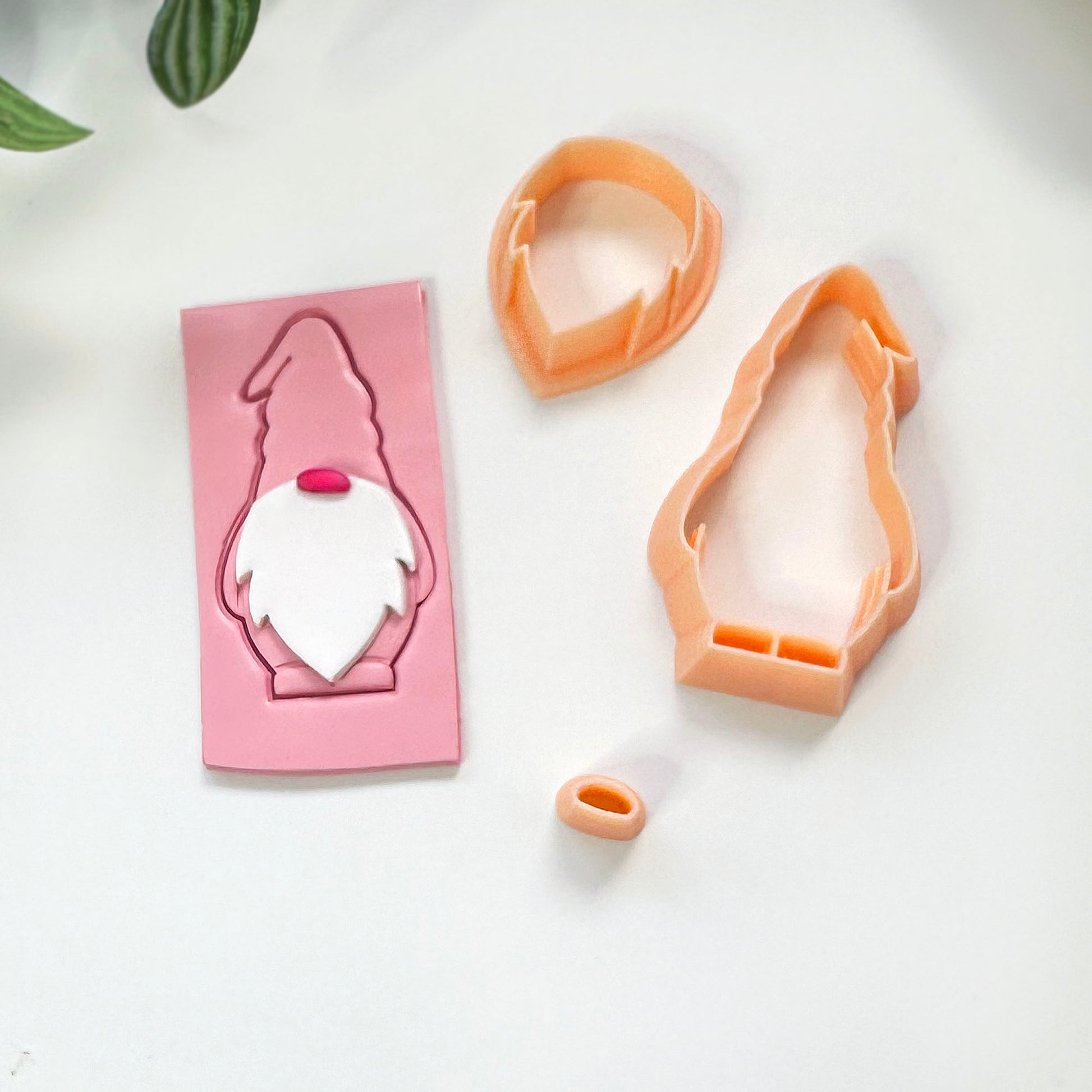 A Christmas gnome cutting set featuring a three piece clay cutter set with a gonk design, Next to the clay uctters is a pink gonk cut out arranged on a clean white background.