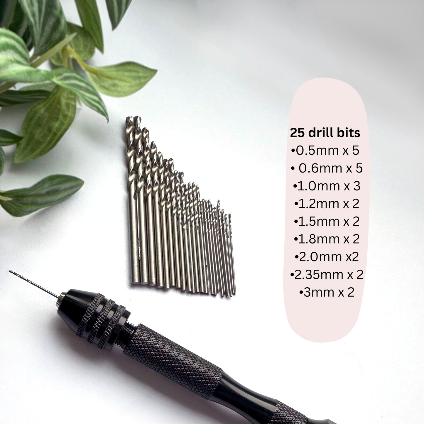 Set of drill bits with a drill on a white surface with green leaves.