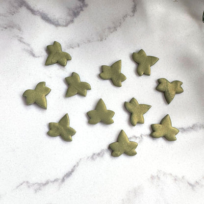 Nine small olive green ivy-shaped craft clay cut outs scattered on a white marble surface.