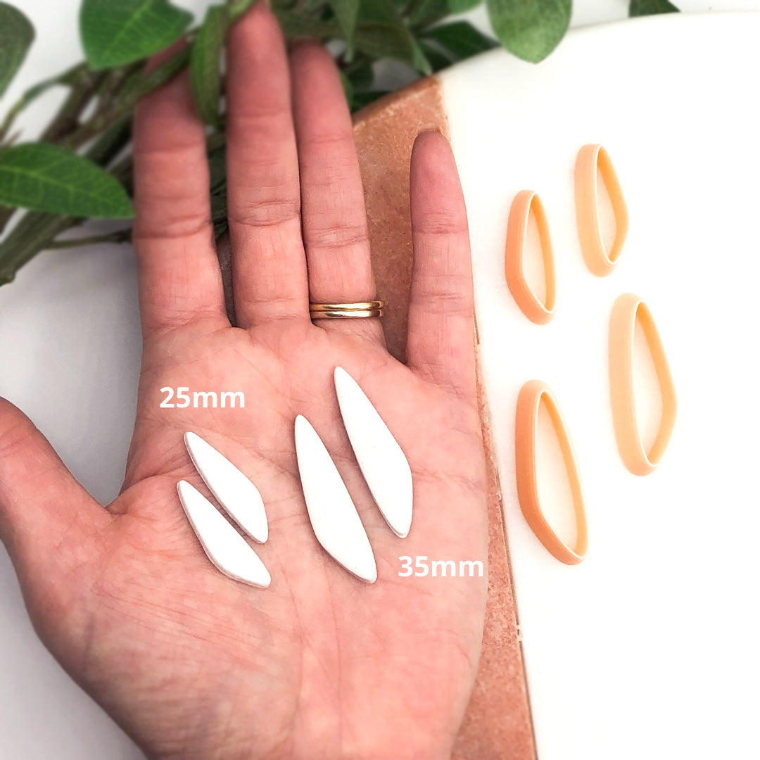 organic slim drop clay cutter, shown as a mirror set. Two clay cut outs on a hand then two mirroed peach clay cutters on a marble tray with green leaves in the background. Sizes shown are 25mm and 35mm