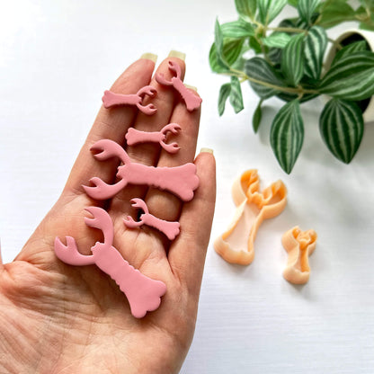 hand holding pink polymer lobster cut outs in 25 and 50mm and the lobster shape clay cutter - on a light surface with green leaves in the background