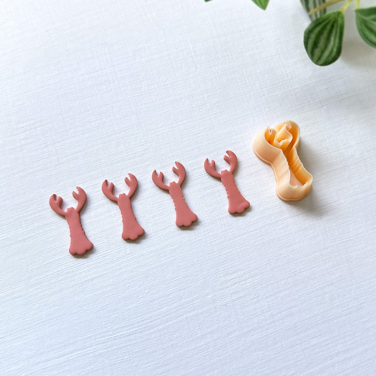 Pink polymer lobster cut out and the lobster shape clay cutter - on a light surface with green leaves in the background