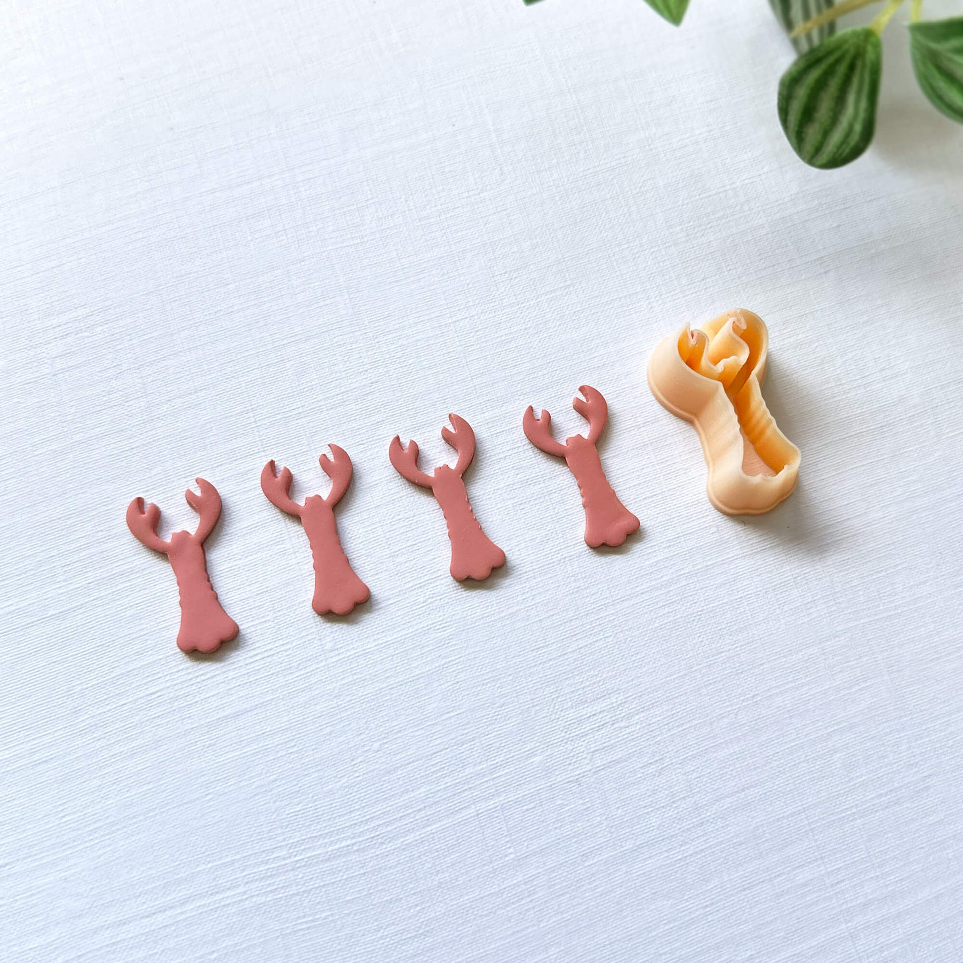 Pink polymer lobster cut out and the lobster shape clay cutter - on a light surface with green leaves in the background