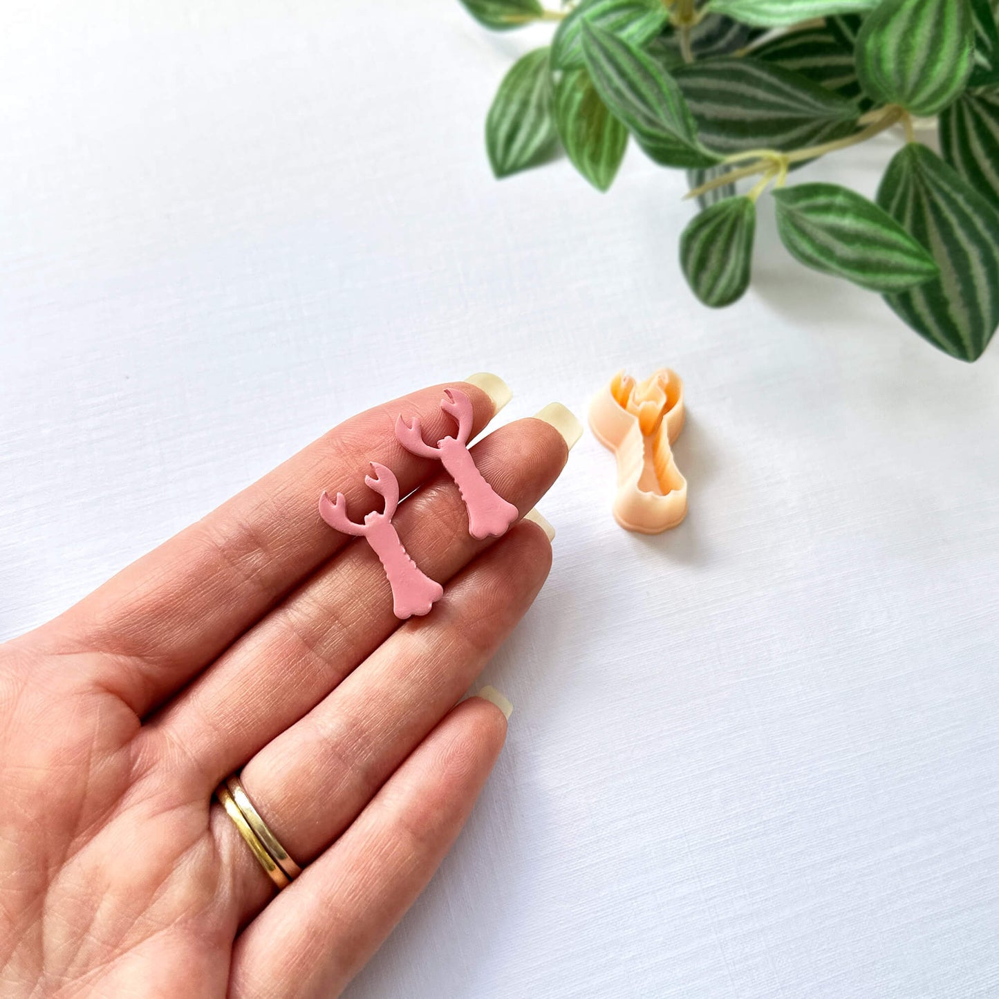Pink polymer clay 25mm lobster cut out s and the lobster shape clay cutter - on a hand for size reference with green leaves in the background