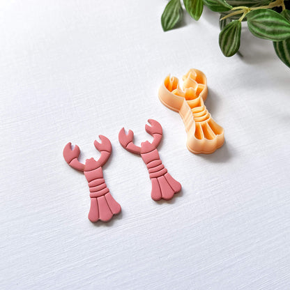 Peach lobster-shaped clay cutter and the pink polymer clay cut out on a light surface with a plant in the corner.