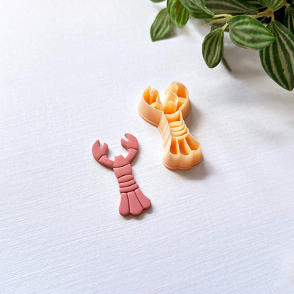 Peach lobster-shaped clay cutter and the pink polymer clay cut out on a light surface with a plant in the corner.