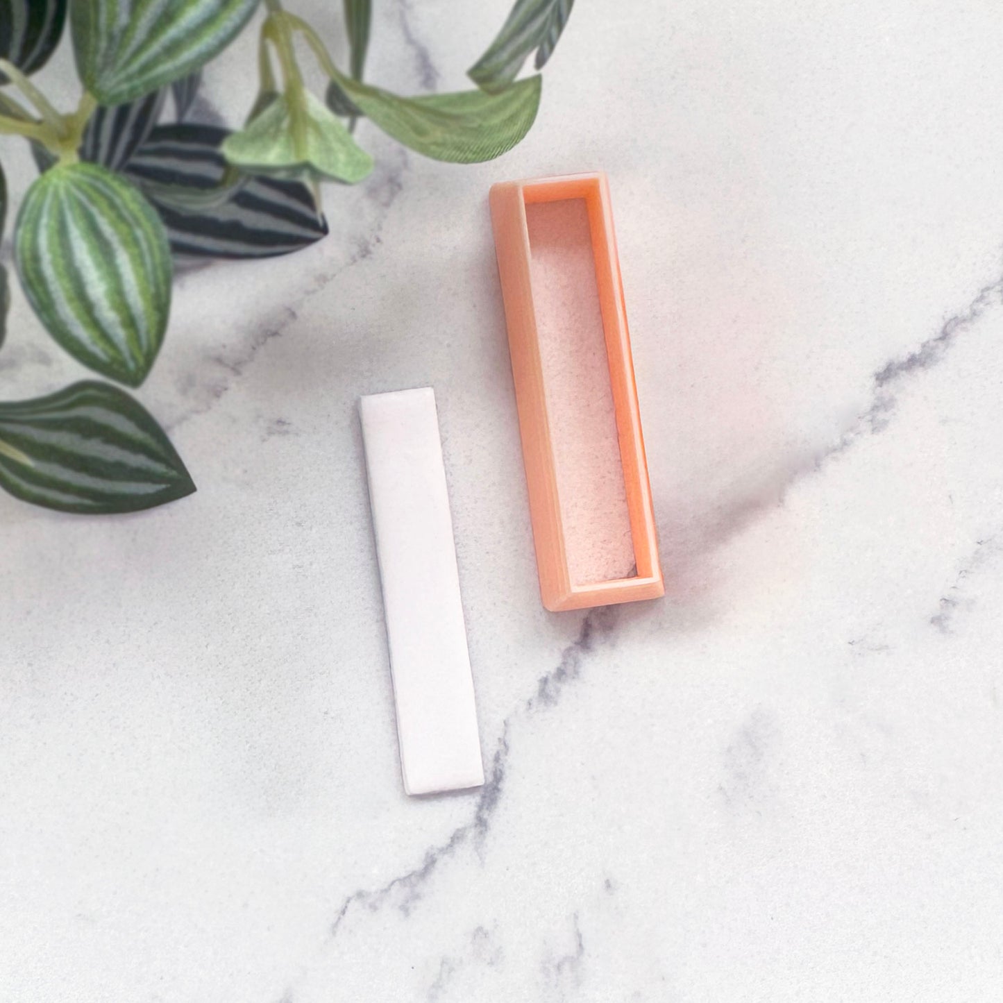 small white rectangular Polymer clay bar, with a peach-colored rectangular clay cutter beside it on a white surface.