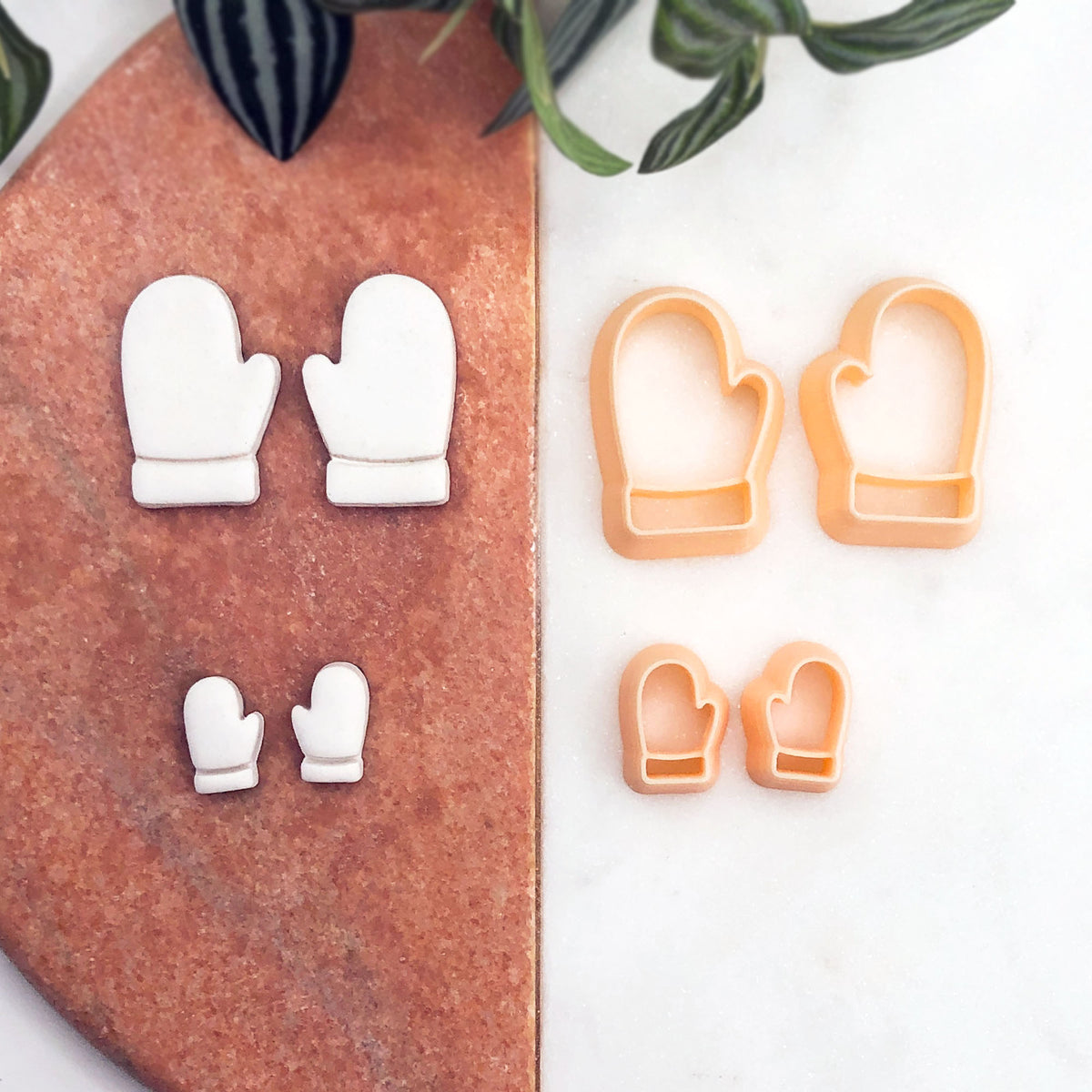 2 mirror sets of small white mitten-shaped clay cut outs, with two peach-colored mitten-shaped cookie cutters placed on a white surface nearby. 