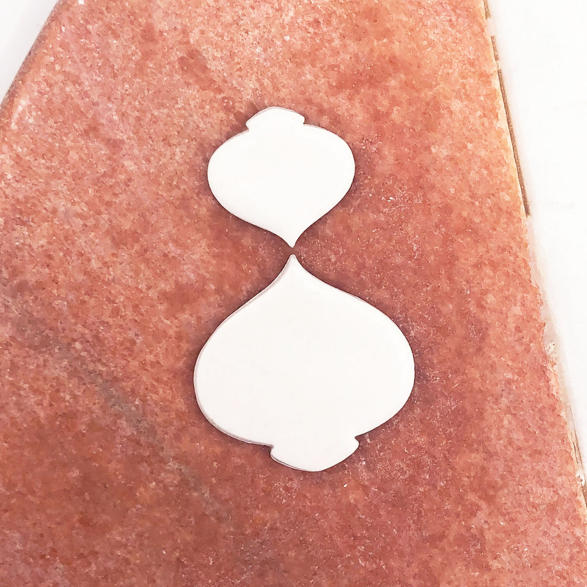 Two small white bauble-shaped clay cut outs displayed on a textured terracotta-colored stone surface.