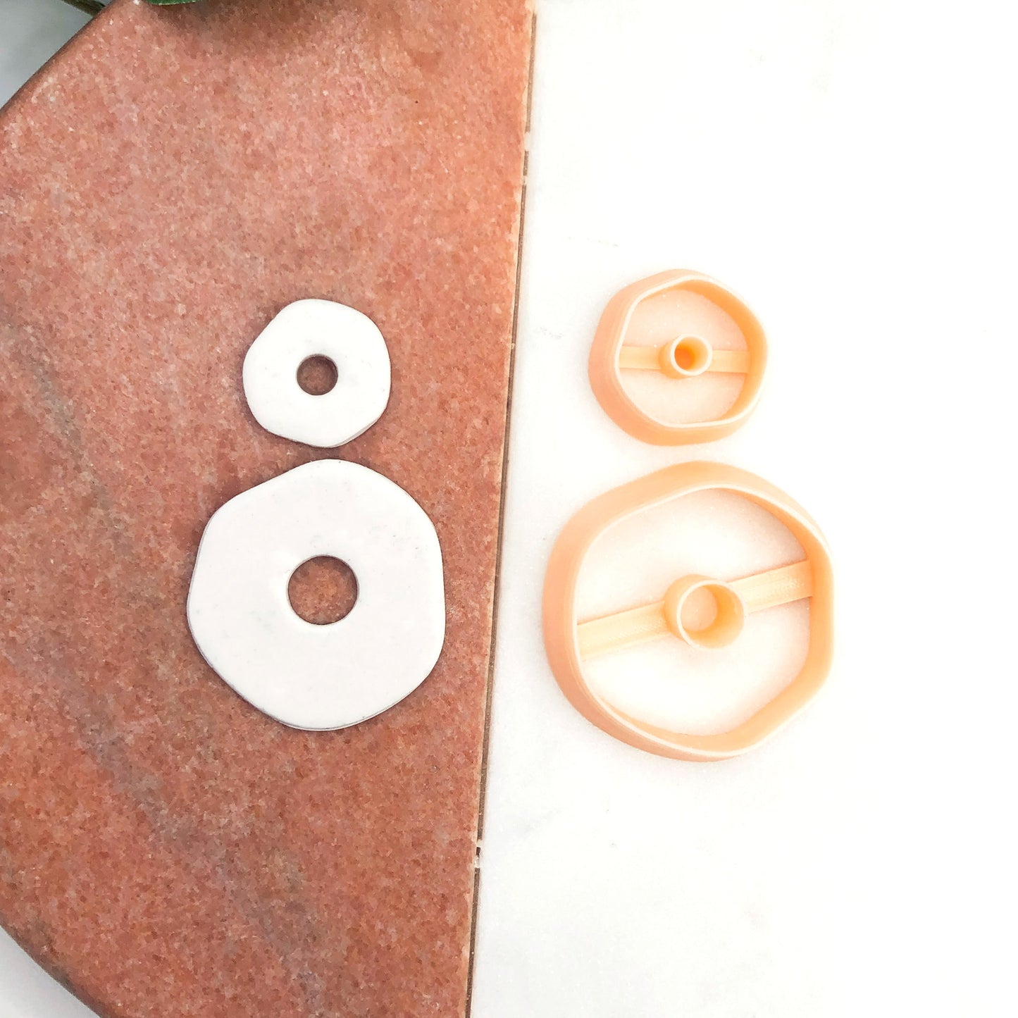 A set of peach-colored plastic clay cookie cutters shown next to two white  organic circular polymer clay cutouts on a split brown-and-white background.