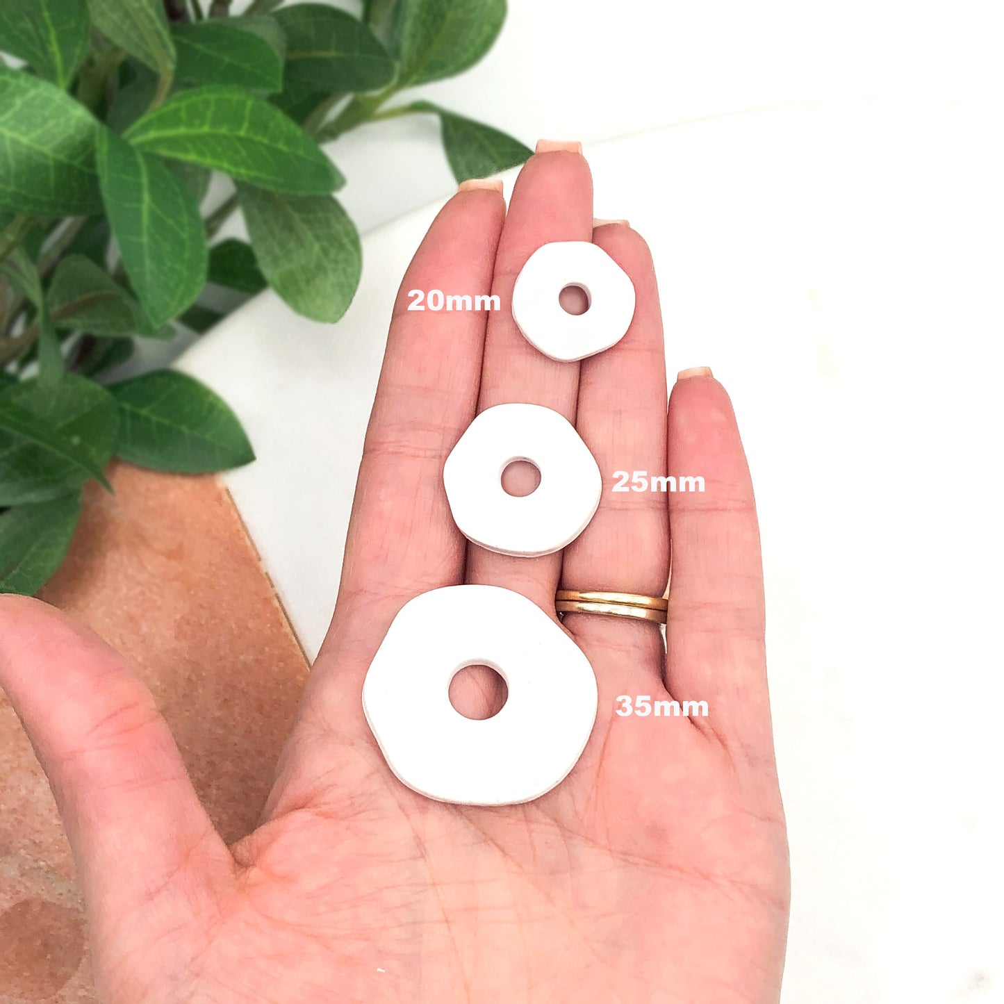 Three white flat organic circular polymer clay pieces shown in a person's hand, labeled 20mm, 25mm, and 35mm, with green leaves in the background.