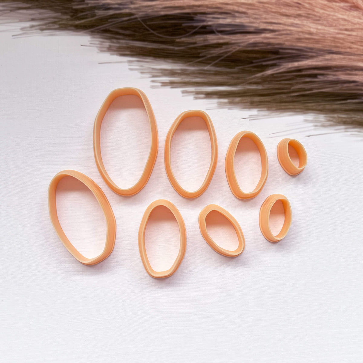 A set of peach-colored 3d printed clay organic oval cutters in various sizes, arranged on a white textured surface 