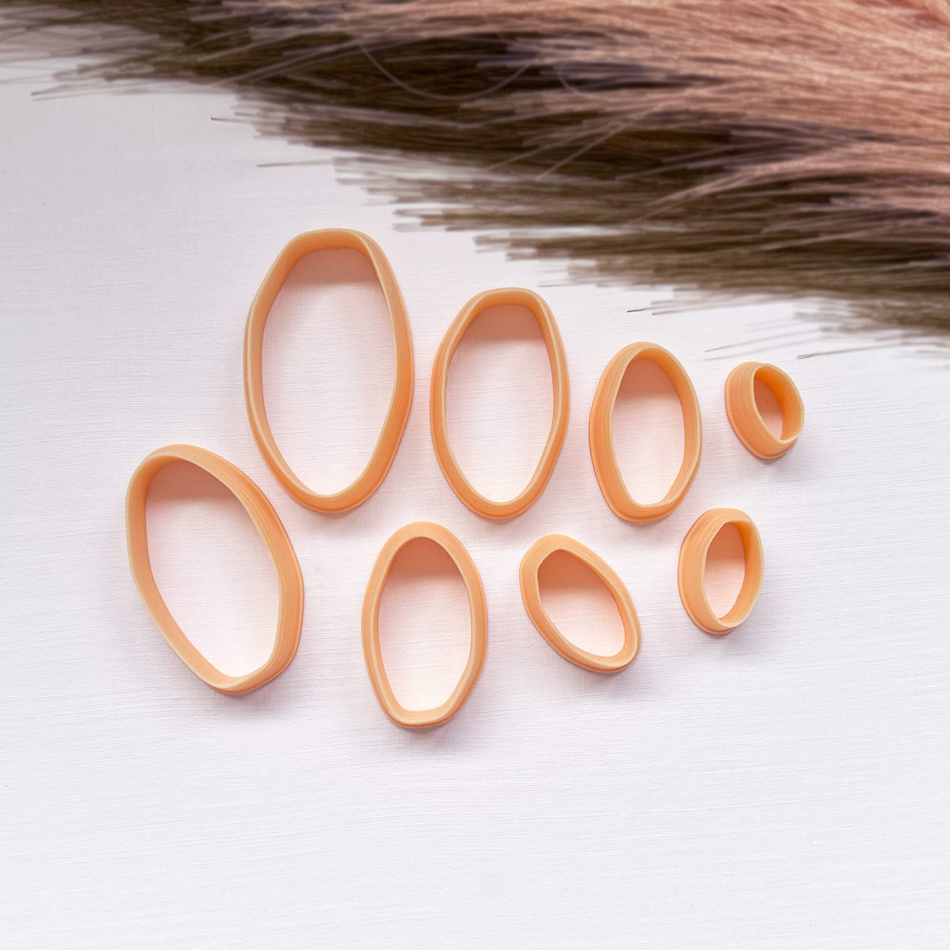 A set of peach-colored 3d printed clay organic oval cutters in various sizes, arranged on a white textured surface 
