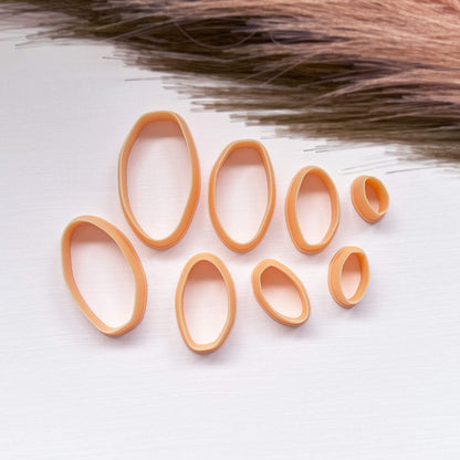 A set of peach-colored 3d printed clay organic oval cutters in various sizes, arranged on a white textured surface 