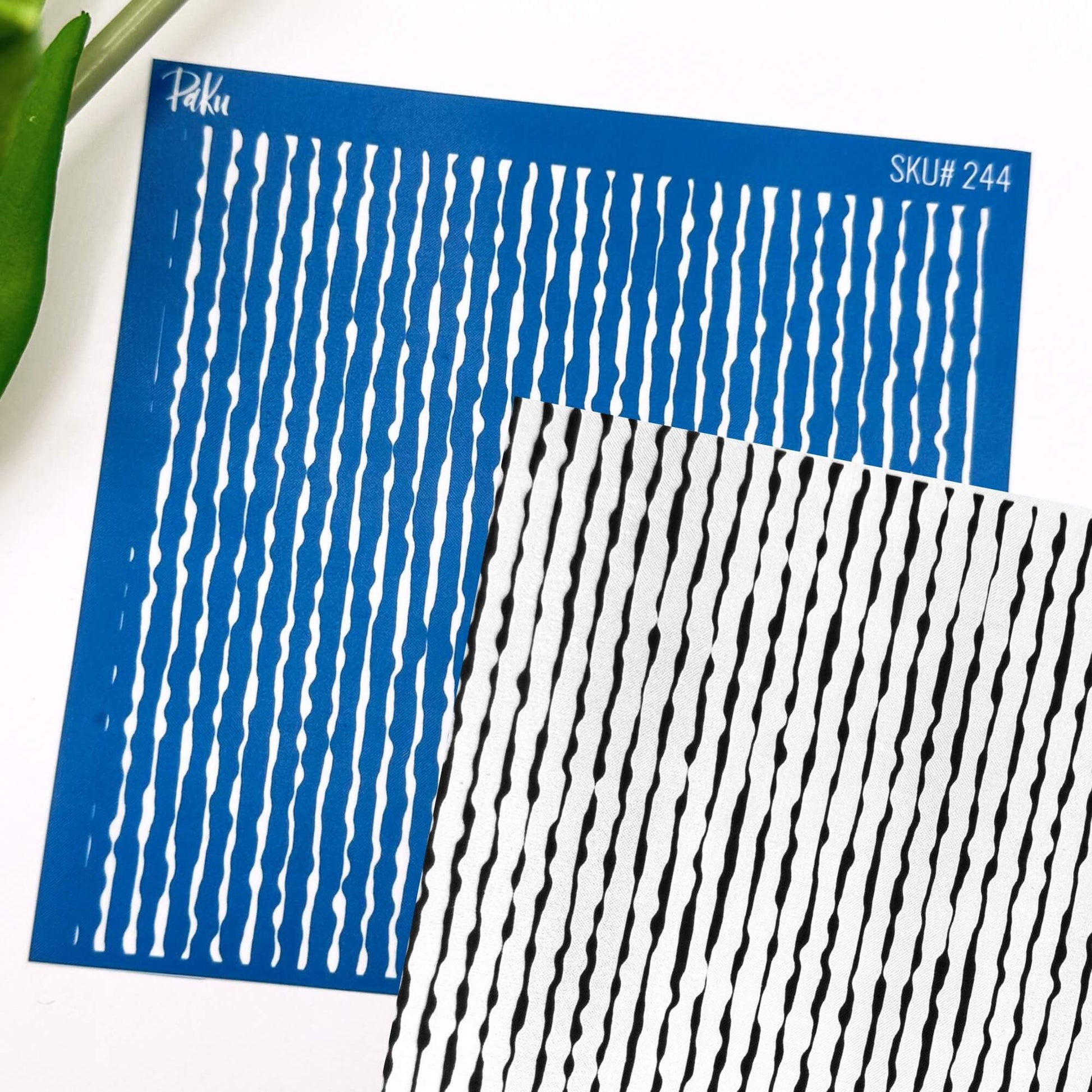 Two patterned silkscreen sheets with vertical wavy stripes, one blue with white stripes and one white with black stripes, shown on a white background with a green leaf edge visible.