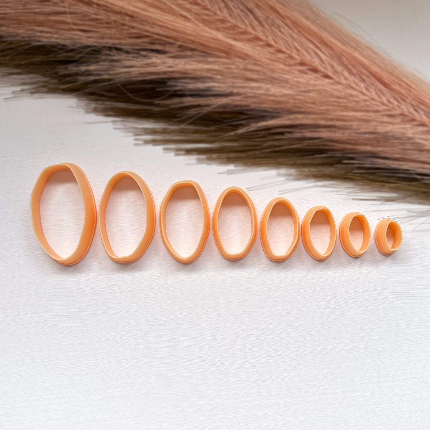 A set of 8 peach-colored 3d printed clay organic oval cutters in various sizes from 50-15mm, arranged on a white textured surface