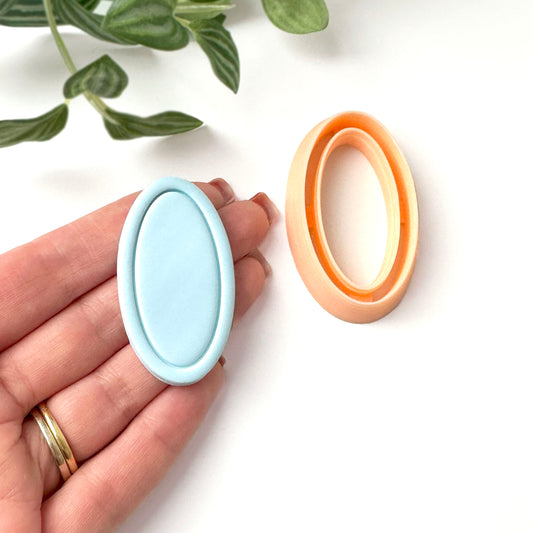 A light blue oval-shaped polymer clay cut out with a framed edge. The mould is held in a hand. A  peach-coloured oval-shaped clay cutter is also shown.