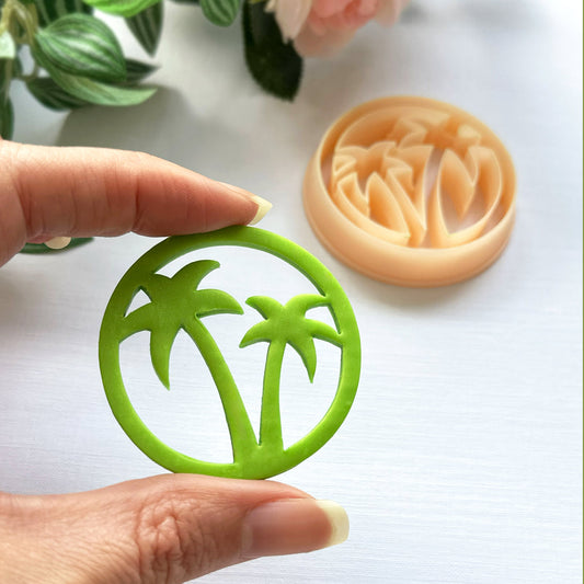 Green palm tree-shaped polymer clay cut out held by a hand  and the clay cutter in the background